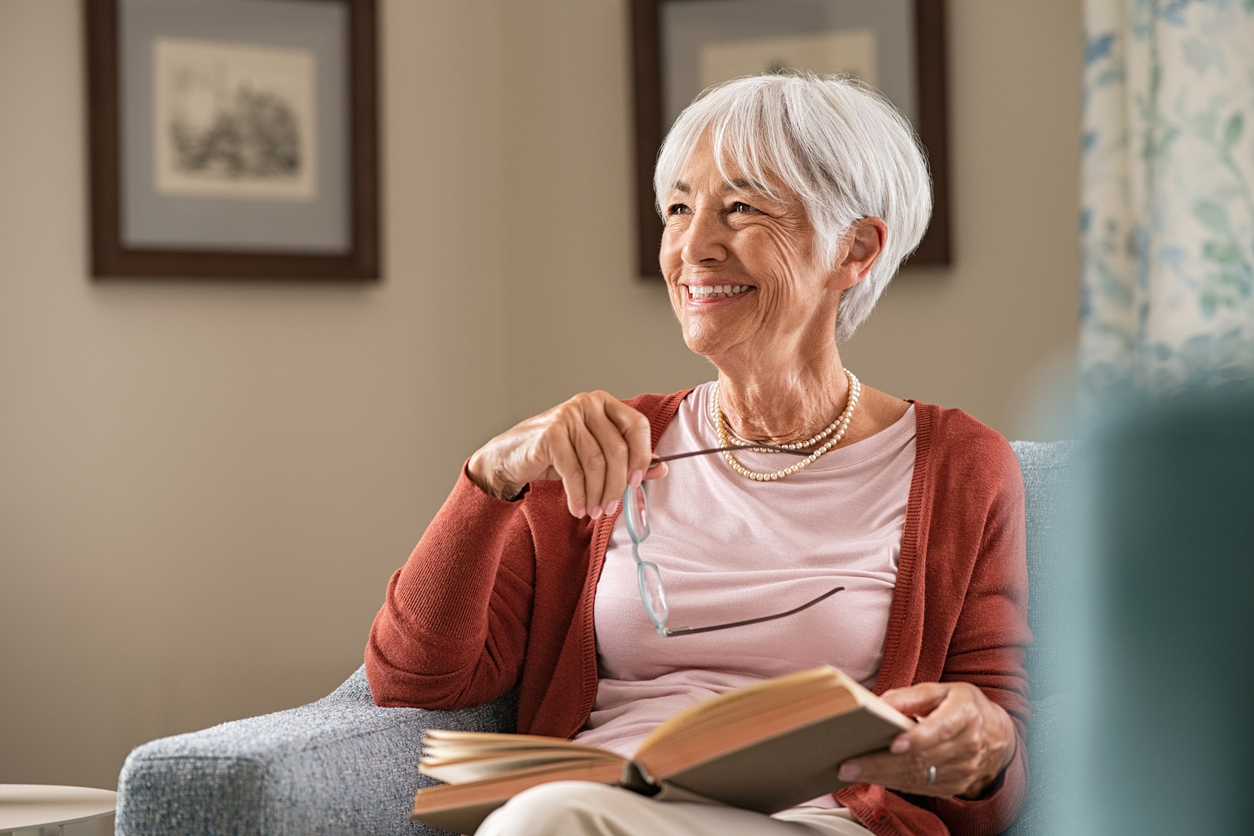 Cheerful senior woman holding book and eyeglasses